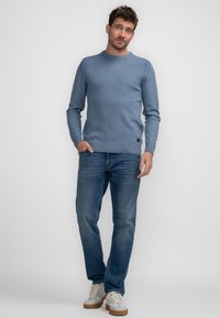 Pulover bleu deschis cu guler rotund, realizat dintr-un material knit moale, prezentând detalii cu model cu nervuri la umeri și manșete, asortat cu blugi albaștri și tenisi bej.