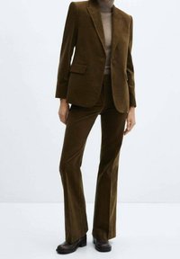 Brązowa marynarka ze sztruksu z klapą z wcięciem, zapinana na jeden guzik, z dwoma przednimi kieszeniami, zestawiona z dopasowanymi, rozszerzanymi spodniami i botkami za kostkę.