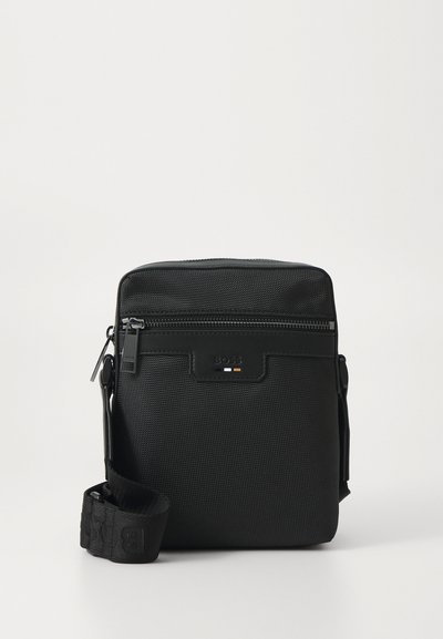 Sac en bandoulière noir en nylon avec une surface texturée, une fermeture éclair, une sangle réglable et un accent de logo en orange et blanc.