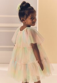 Robe en tulle pastel avec des couches froncées, des manches courtes et un dos en forme de scoop. Le vêtement présente un léger éclat irisé et des accents élastiques.