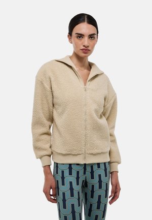 Veste beige zippée en tissu doux et texturé, avec col et manches côtelés. Présente une coupe décontractée et un design sans coutures.