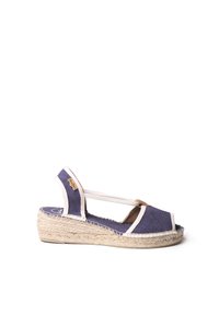 Navy canvas wedge sandaal met witte banden en een geweven jute zool. Beschikt over een open teenontwerp en een bruine leren accent bij de hak.
