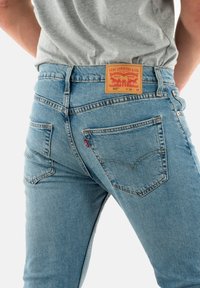 Los jeans Levi's 502 en denin azul claro cuentan con un diseño clásico de cinco bolsillos, costuras en color naranja y un parche de cuero en la parte trasera con la marca.