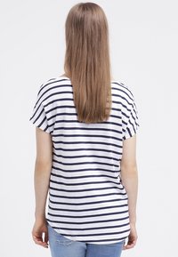 Camiseta de rayas en blanco y marino, con un corte relajado, mangas cortas y un dobladillo redondeado. Costuras visibles en las mangas y el escote.