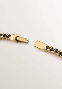 Pulsera de oro con acentos de piedras preciosas negras, textura metálica suave y diseño de cierre rectangular con una banda texturizada.