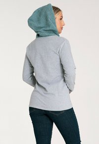 Szary, long-sleeve top z teksturowanym, tealowym kapturem, o dopasowanym kroju i prostym tyle. Materiał wydaje się miękki i casualowy.