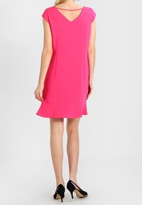 Fuksia lyhyt mekko, jossa on hihansuut, V-mallinen selkäosa ja A-linjainen helma, valmistettu sileästä kankaasta. Mustat korkokengät täydentävät asua.
