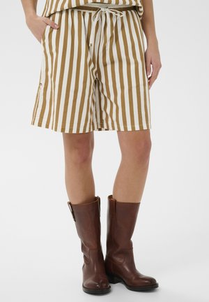 Pantaloni scurți cu dungi bej și maro din bumbac, cu talie elastică și buzunare; asortați cu cizme maro de piele până la genunchi.