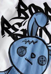 Witte katoenen t-shirt met een blauw konijnafbeelding met knoopogen, gestikt mondje en zwarte graffiti-achtige tekst op de achtergrond.