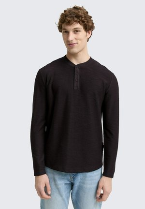 Camisa henley negra de mangas largas con tejido texturizado, cuenta con un cuello redondo y tres botones negros, combinada con jeans de color azul claro.