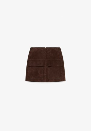 Ruskea mokkanahkainen minihame, jossa on kaksi etutaskua läpällä ja keskellä vetoketjukiinnitys, valkoisella taustalla esitetty.