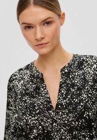 Zwarte blouse met wit gespikkeld patroon, voorzien van een V-hals ontwerp en een losse pasvorm. Gladde textuur, lichtgewicht stof. Geen zichtbare hardware.