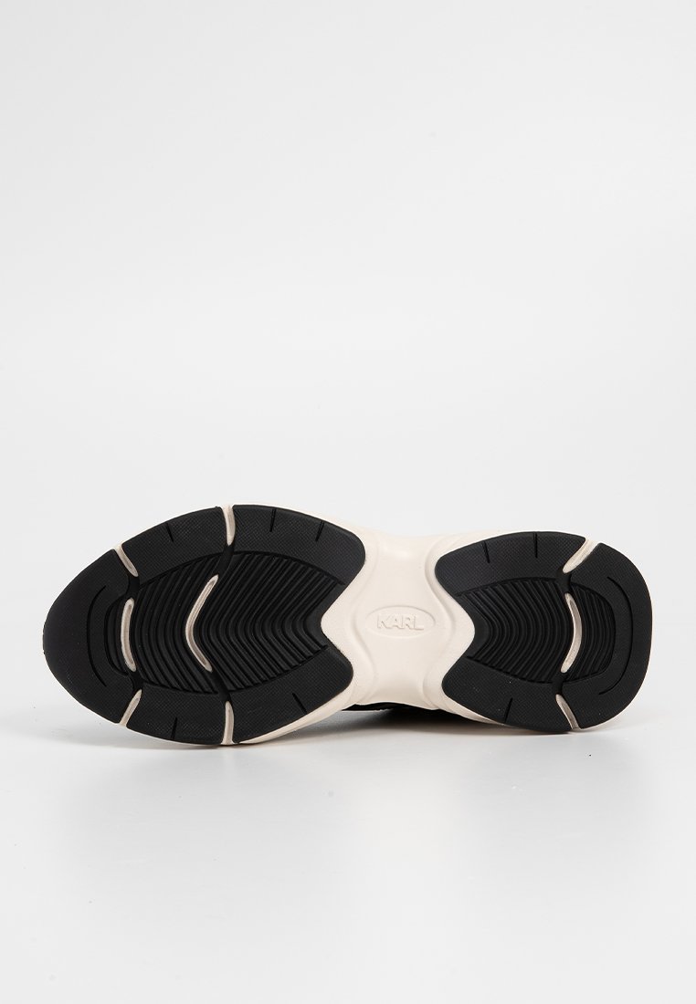 Semelle de sneaker noire en caoutchouc avec une surface texturée, présentant un intercuissard de couleur crème et un logo distinct au centre.