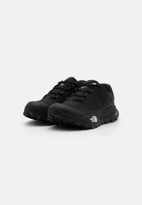 Zapatillas de trail running negras con diseño de cordones, suela de goma texturizada, áreas reforzadas y acentos de marca en el costado.