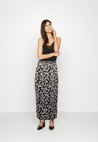 Top preto sem mangas com acabamento em renda, combinado com uma saia longa preta com um padrão floral branco; modelo usa sapatos de salto pretos.