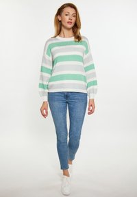 Maglione a righe in verde menta e bianco, texture lavorata a maglia, maniche larghe, abbinato a jeans blu aderenti e sneakers bianche.
