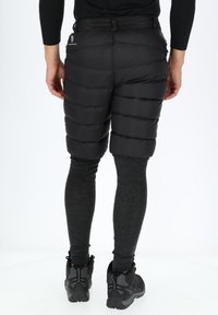 Zwarte puffer shorts met een gequilt ontwerp, voorzien van een hoge tailleband en zijknippers, gecombineerd met grijze legging en wandelschoenen.