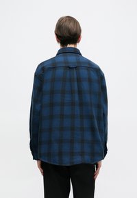 Μπλε και μαύρο καρό πουκάμισο φλιάντ με γιακά, μακριά μανίκια και στρογγυλή γραμμή, διαθέτοντας μαλακή υφή υφάσματος και λεπτομέρεια στο πίσω μέρος.