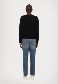 Zwarte gebreide trui met een ronde hals, gecombineerd met lichtblauwe spijkerbroek. De pasvorm is ontspannend en de broek heeft een vervaagde wassing.