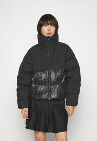 Zwarte pufferjack met hoge kraag, glanzend nylon paneel op de taille en ritsluiting. Bevat een klassiek logo op de borst.
