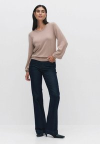 Ljus beige, långärmad stickad tröja i kombination med mörk denim flare jeans. Tröjan har en rund halsringning och jeansen har synliga sömdetaljer.