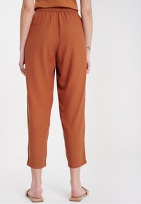 Kalhoty barvy rezavě hnědé, lehké s elastickým pasem, vykrojený střih nohavic a dvěma zadními kapsami. Vyrobené z měkké, prodyšné látky.