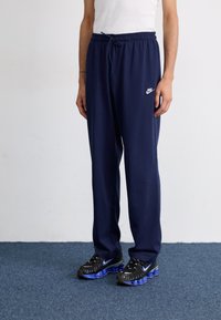 Marine joggebukser har elastisk midjebånd med snøring og en hvit Nike-logo. Kombinert med svarte joggesko med blå detaljer.