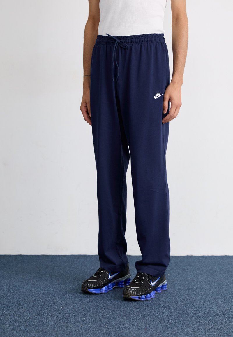 Marine joggebukser har elastisk midjebånd med snøring og en hvit Nike-logo. Kombinert med svarte joggesko med blå detaljer.
