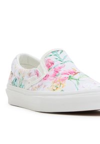 Basket blanche sans lacets avec imprimé floral rose, jaune et vert et épaisse semelle blanche en caoutchouc, inclinée vers la gauche sur fond blanc.
