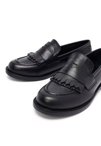 Mocassins en cuir noir avec un détail de frange et de pampilles, bout arrondi et accents cousus. Texture lisse avec un design épuré et minimal.