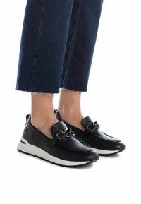 Mocasines de cuero negro con un upper texturizado y un acento decorativo de cadena. Presentan una suela de color claro y un diseño de punta redondeada.