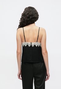 Czarna jedwabna halka z koronkową lamówką wzdłuż dekoltu, regulowanymi ramiączkami i luźnym krojem, zestawiona z czarnymi satynowymi spodniami.