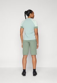 Top de manga corta verde claro con acentos en verde más oscuro y pantalones cortos a juego. Tela suave y casual, diseño minimalista sin logotipos visibles.