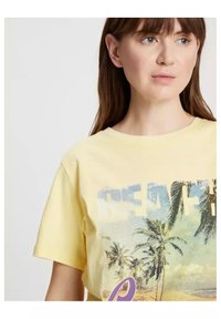 Żółta bawełniana koszulka z grafiką plaży, przedstawiającą palmy oraz słowo "BEACH" w stylizowanej czcionce. Krótkie rękawy i okrągły dekolt.