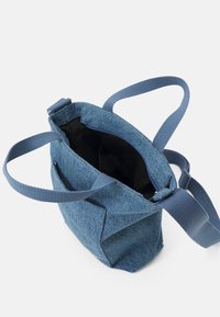 Denim tote bag with a structured shape and dual handles. Features a dark interior and contrasting blue straps. No visible hardware.