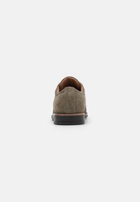 Zapatos de ante en verde oliva con ribete de cuero marrón y suela negra. Presentan un tacón redondeado y una plantilla texturizada. Se muestra la vista trasera.