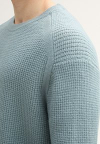 Jasnoniebieski sweter z dzianiny z fakturowanym wzorem, okrągłym dekoltem oraz ściągaczami na ramionach i mankietach. Miękka, oddychająca tkanina.