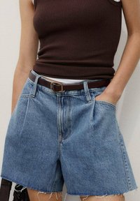 Ljusblå denimshorts med fransad nederkant, hög midja, framfickor och ett brunt läderbälte med ett guldspänne.