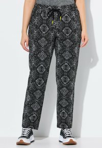 Pantalons noirs avec un motif texturé serpent en gris. Dotés d'une taille à cordon coulissant, d'une coupe ample et portés avec des baskets noir et blanc.