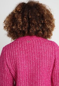 Maglione rosa lavorato a maglia con un motivo testurizzato, caratterizzato da un colletto a costine e un piccolo logo metallico sul retro.