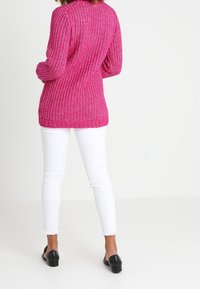 Maglione lavorato a maglia magenta con vestibilità ampia, polsini e orlo a costine, abbinato a jeans skinny bianchi e scarpe slip-on nere.