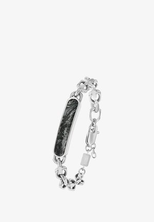 Bracelet en chaîne argentée avec un pendentif en pierre noire rectangulaire, présentant une surface texturée et des maillons en métal poli.