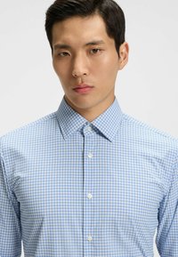 Camicia a scacchi blu chiaro realizzata in un tessuto morbido, con colletto a punte e bottoni bianchi, design aderente, con motivo a piccoli scacchi.