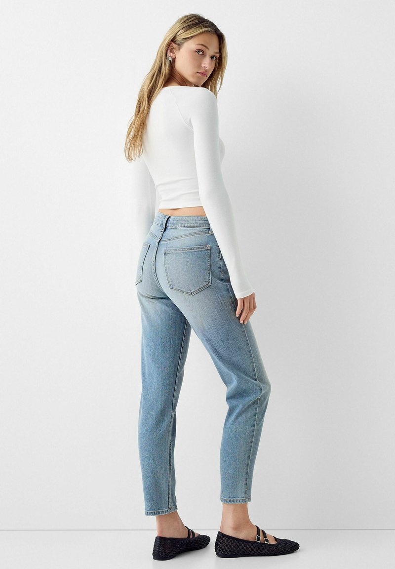 Jeans blu chiaro a vita alta con gamba affusolata, dotati di due tasche posteriori e dettagli di lavaggio delicati, abbinati a un top aderente a manica lunga bianco.