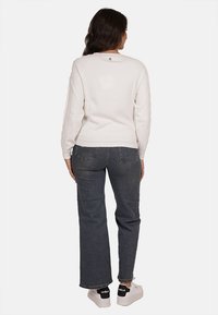 Maglione bianco a maglia con maniche texture, scollatura rotonda e un piccolo bottone sul retro, abbinato a jeans scuri in denim e sneakers bianche.