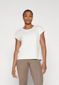 T-shirt blanc ajusté léger avec des manches courtes et un col rond ; associé à des leggings marron ; texture lisse, branding minimal.