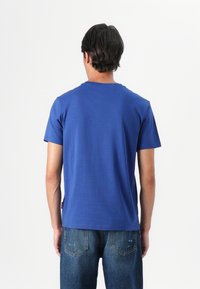 T-shirt in cotone blu con maniche corte e colletto tondo, caratterizzato da una texture liscia e un orlo dritto, indossato con jeans in denim.