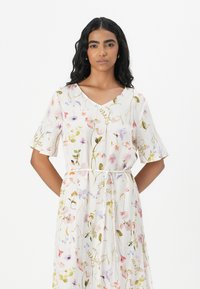 Blomsterprintet kjole med V-hals, korte ærmer, cinchet talje med bånd og et let, tekstureret stof i pastelfarver.