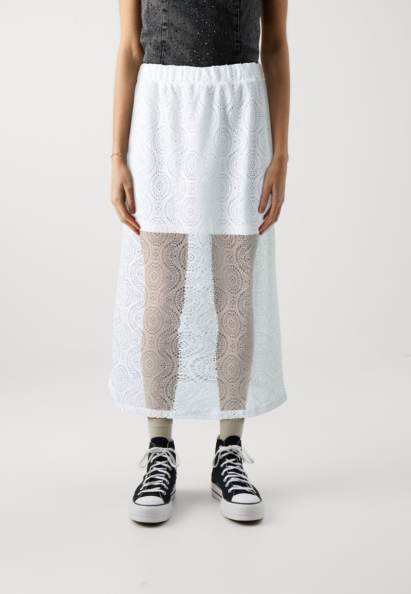 Hvit blonde maxi skjørt med elastisk midjebånd, har et mønstret design og gjennomsiktige seksjoner. Brukt med svarte høye sneakers.