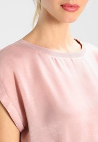 Top rosa a maniche corte con una texture liscia e lucida e scollatura rotonda. Include una leggera arricciatura vicino alla scollatura e una vestibilità rilassata.